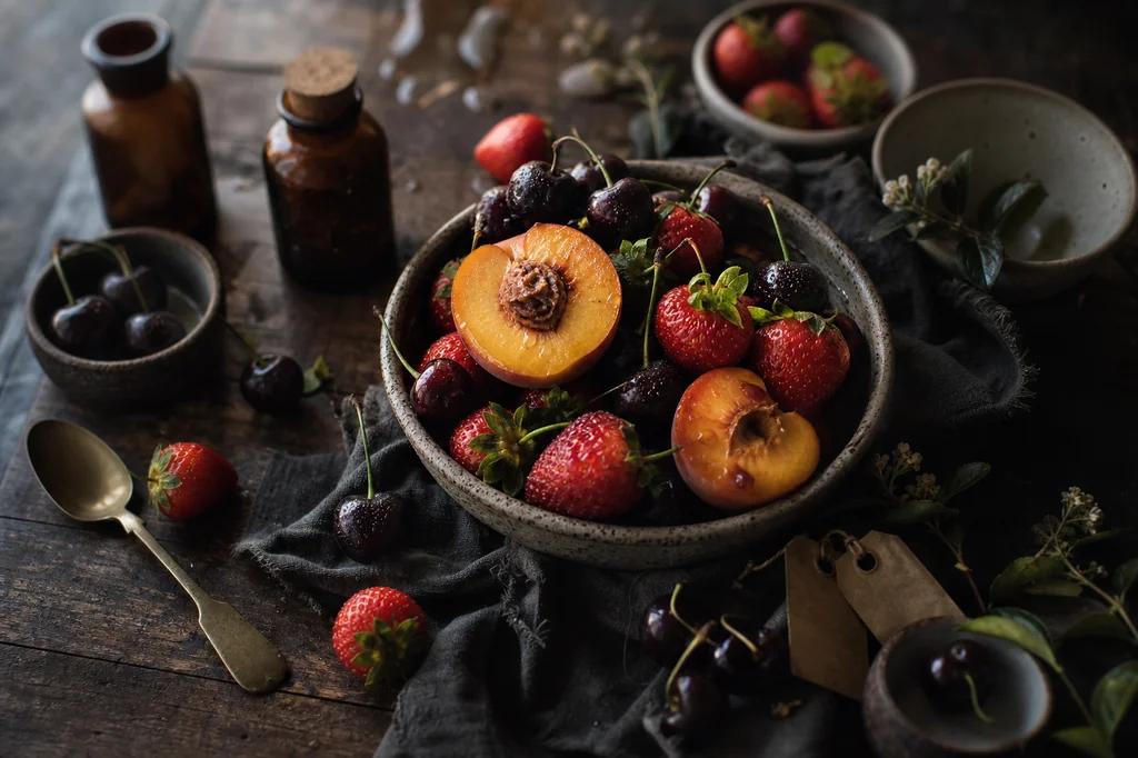 A stoneware bowl of strawberries, halved peaches and dark cherries on a rustic wooden table